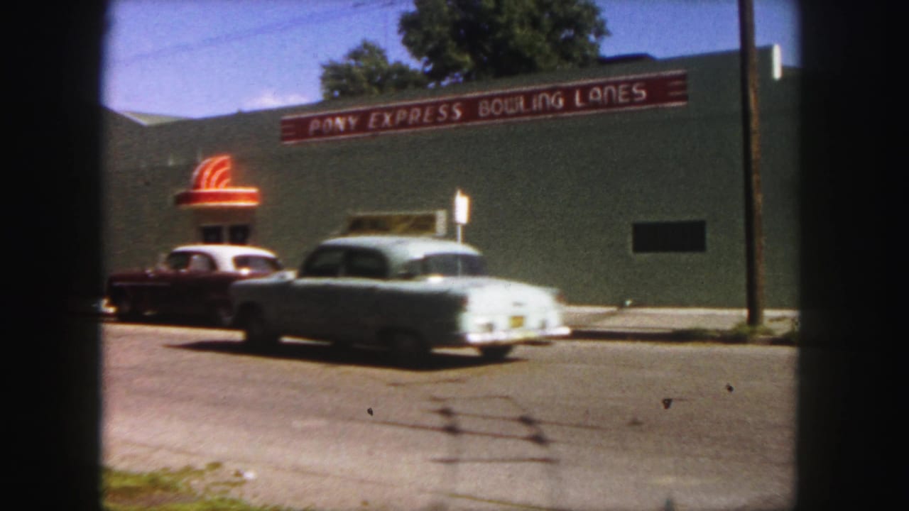 1958 Denver street view with a light blue car moving past the Pony Express Bowling Lanes exterior.