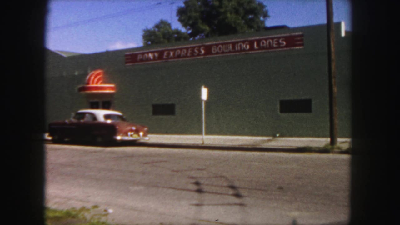 A red and white mid-century car sits outside Pony Express Bowling Lanes in Denver, with the sign visible above.