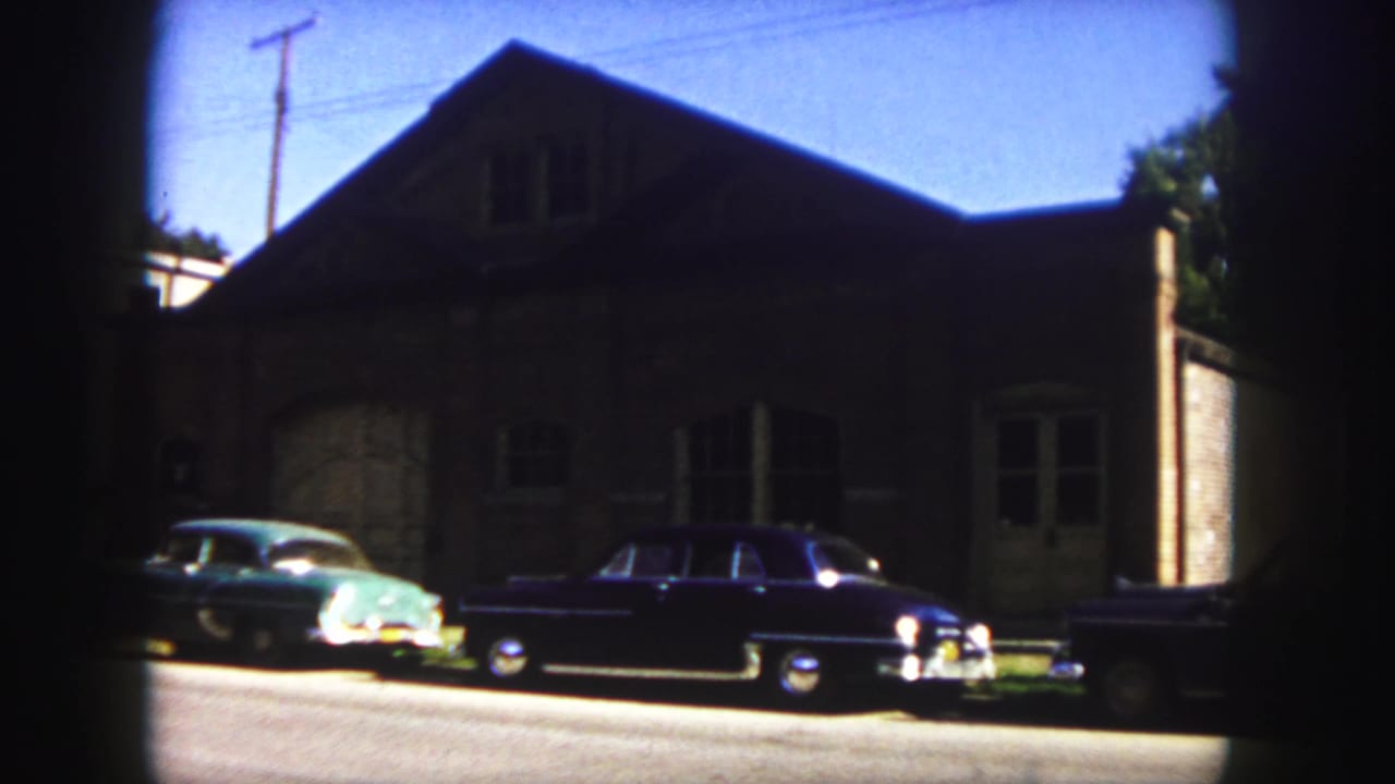 Parked vintage cars and a shadowed brick facade viewed from across the street.