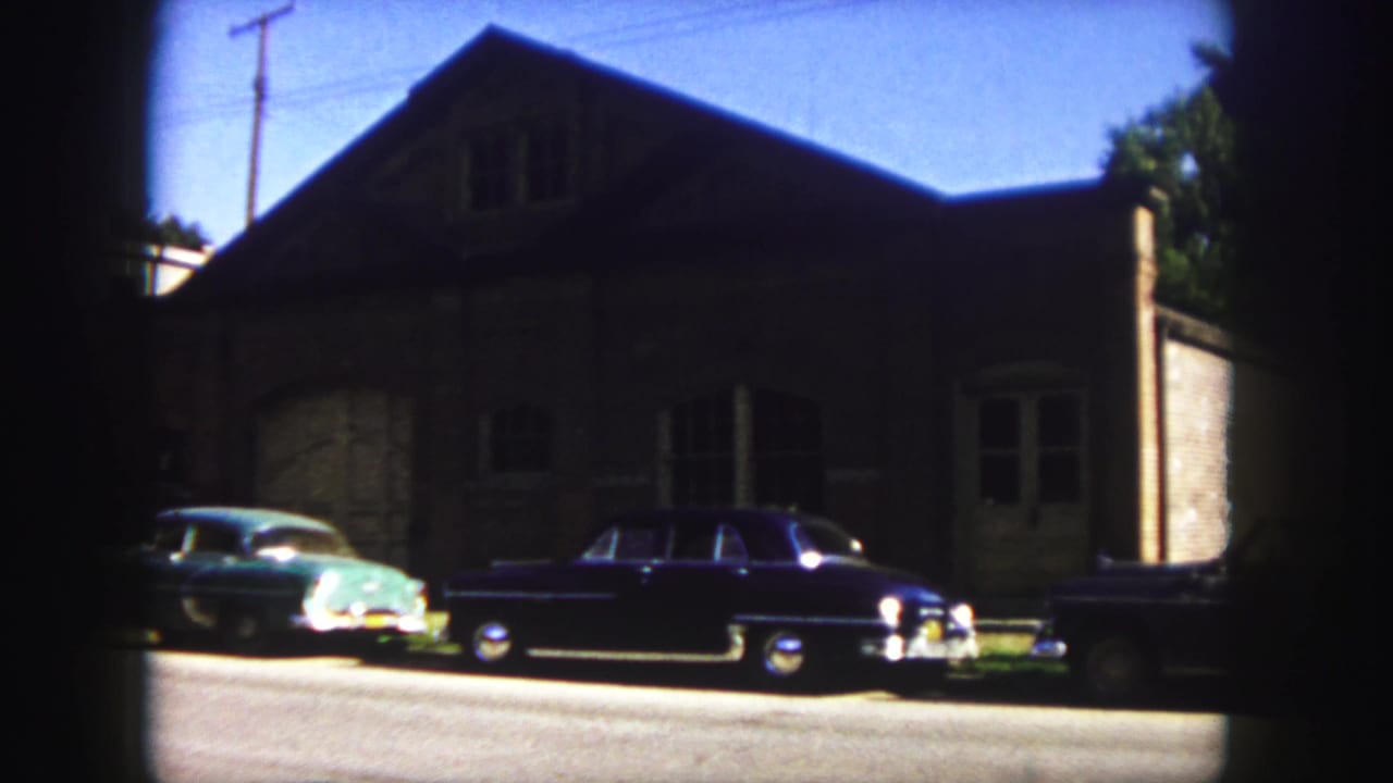 Two parked cars beside a large shadowed building with a roofline and utility pole.