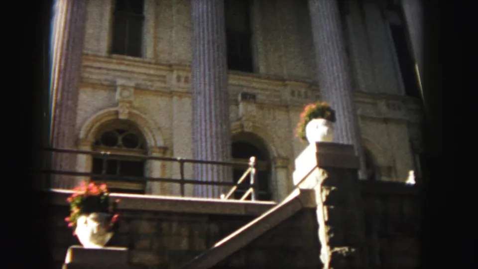 1958 Denver home-movie frame of a grand columned facade, stone stair rail, arched windows, and potted flowers.