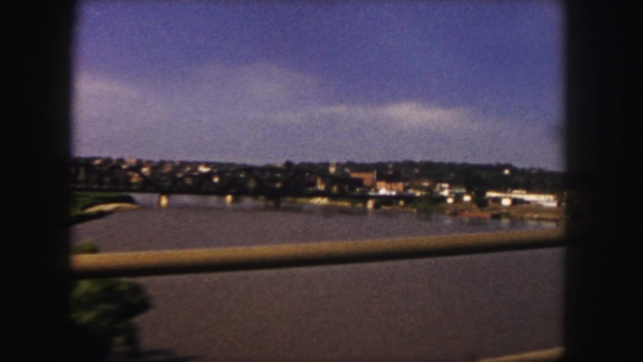 Water and a distant shoreline seen from a moving vehicle with a rail in the foreground.