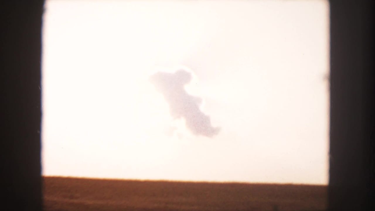 Open field beneath a bright pale sky with a distinct cloud formation near the center.