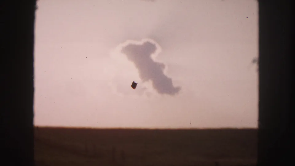 1958 8mm Denver-area landscape frame with a low field, pale sky, cloud formation, and visible film dust.