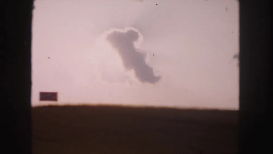 1958 8mm landscape near Denver with a dark field, hazy sky, central cloud, and small rectangular mark near the horizon.