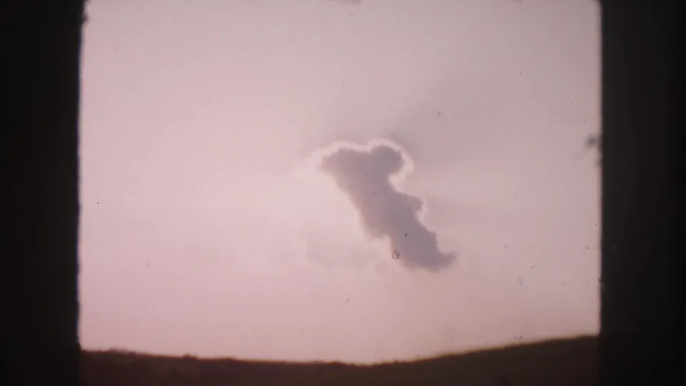 1958 Colorado road-trip footage frame with a soft cloud formation floating above a low, dark horizon.