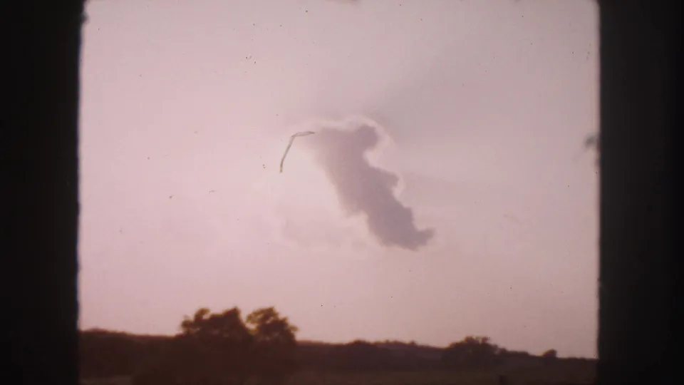 1958 8mm travel frame showing a hazy cloud form over distant trees and open horizon near Denver, Colorado.