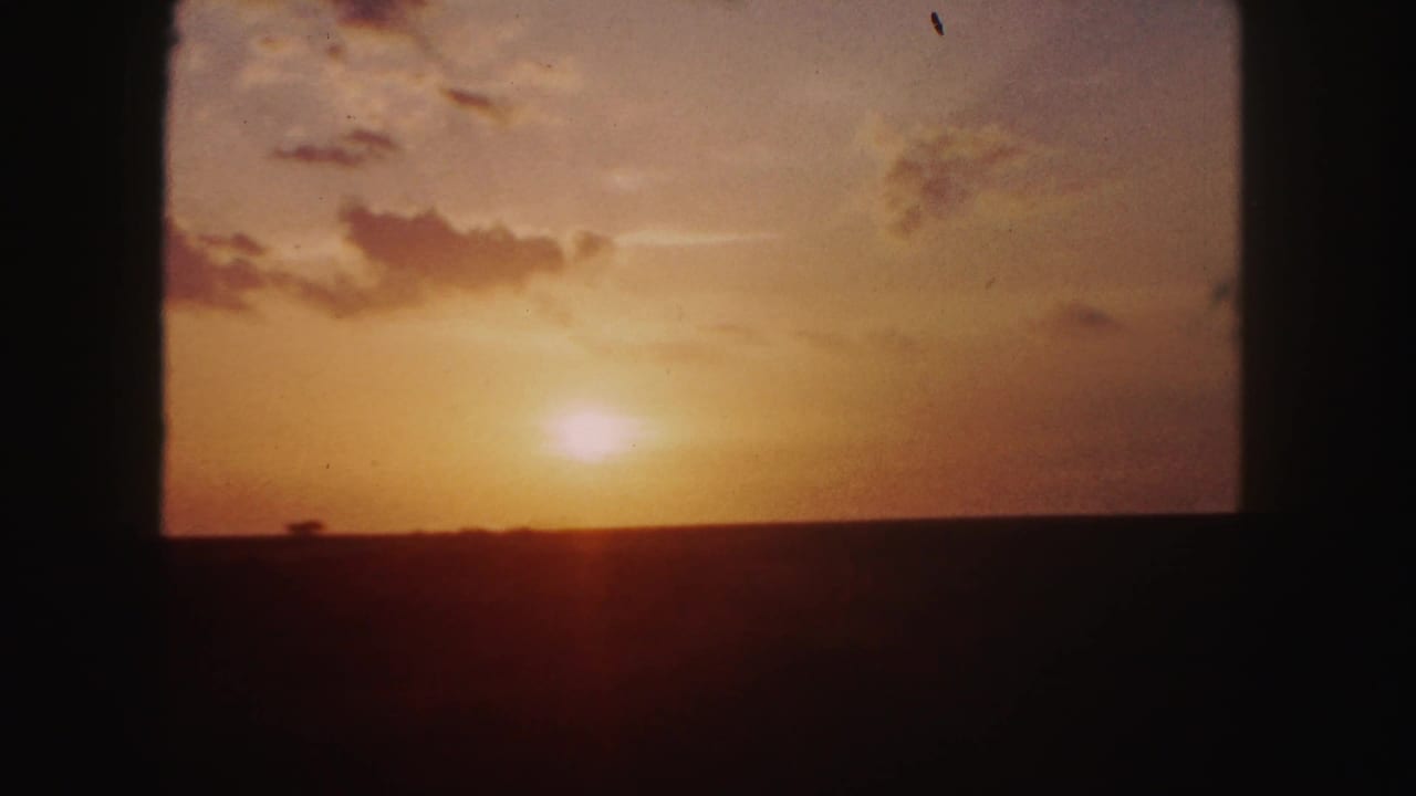 1958 8mm home-movie view near Denver showing a low sun, amber sky, scattered clouds, and dark window framing.