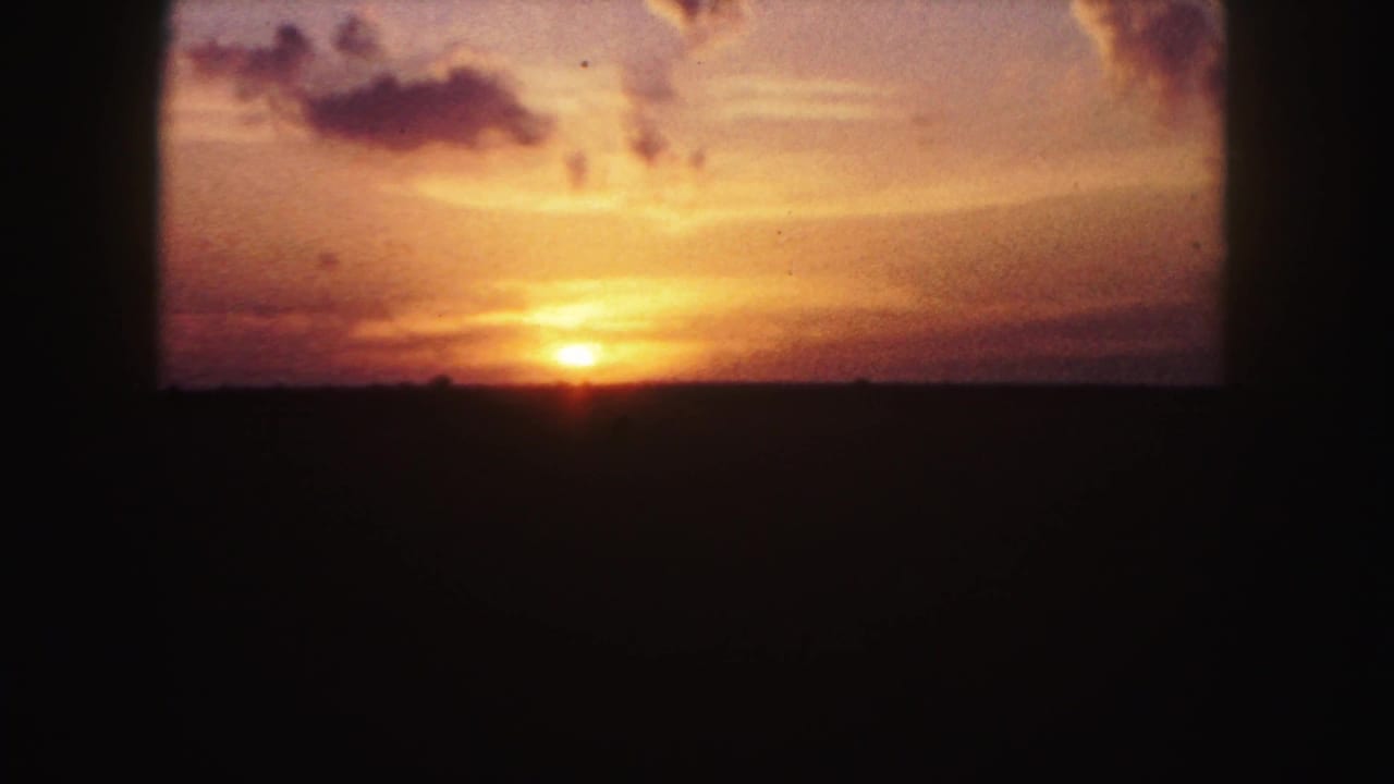 1958 Denver-area 8mm frame showing a small orange sunrise over a dark landscape with warm sky and scattered clouds.