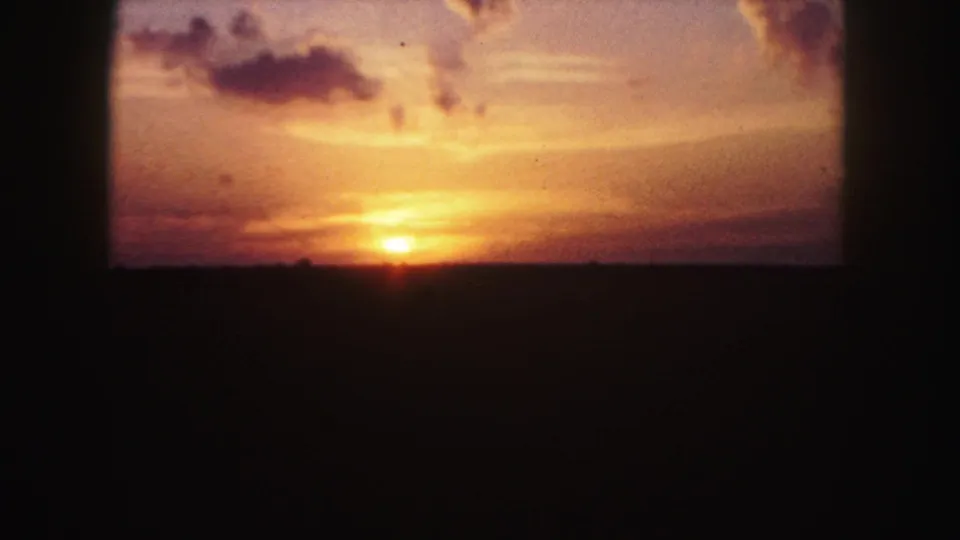 1958 Denver-area 8mm frame showing a small orange sunrise over a dark landscape with warm sky and scattered clouds.