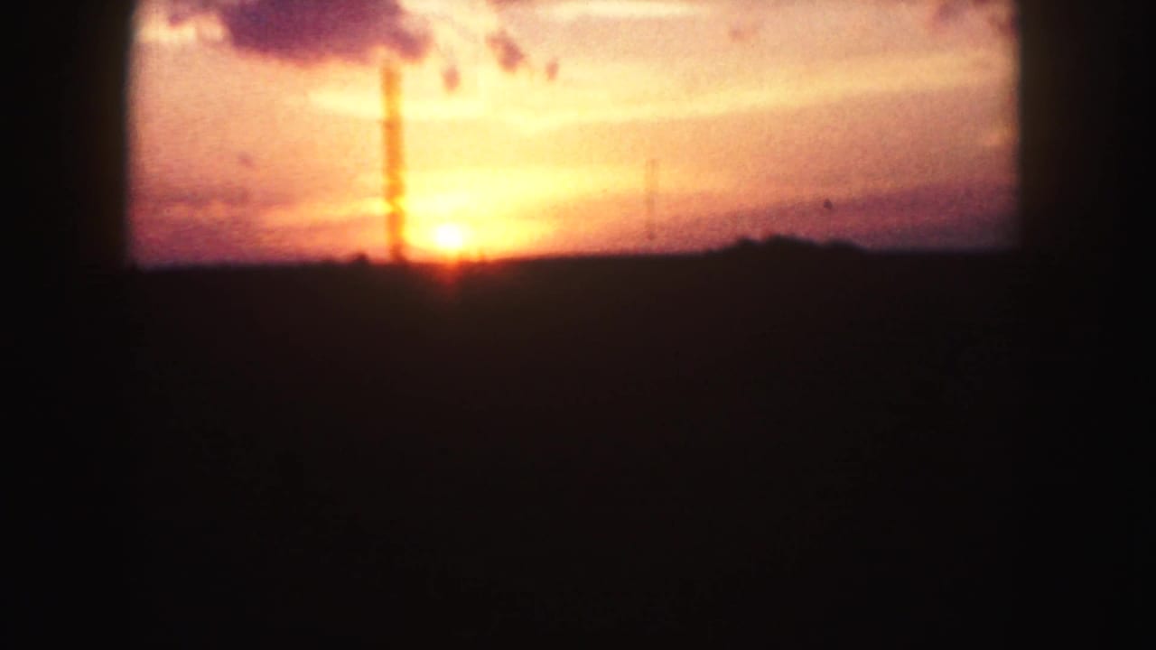 Bright sunrise near the horizon with silhouetted land and cloud shapes in a warm sky.