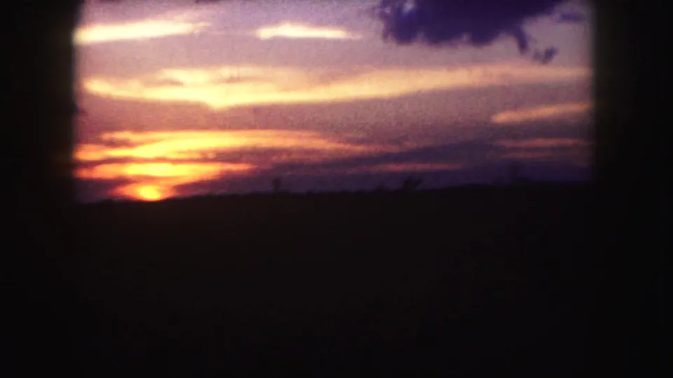 1958 Denver-area 8mm frame showing a glowing sunrise partly low in frame with layered clouds and a dark open foreground.