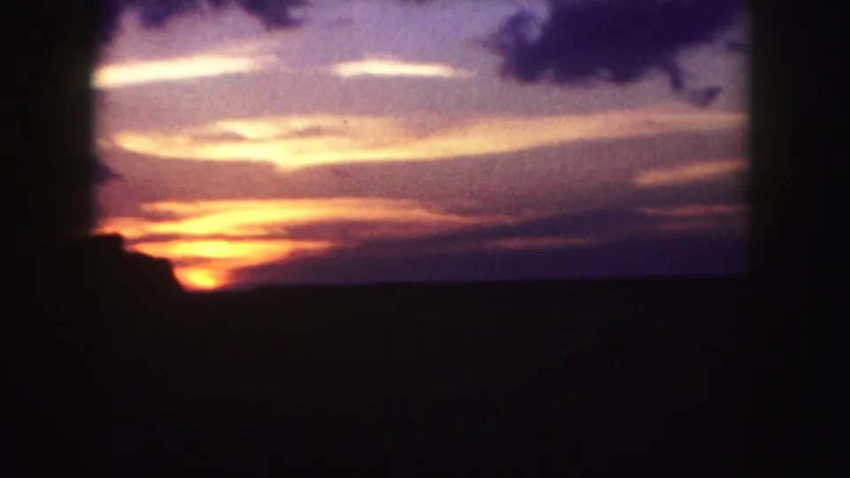 1958 Denver-area 8mm frame with orange sunrise light, purple cloud bands, and a low silhouetted horizon.