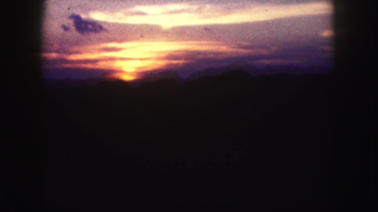 Bright sun near the horizon with dark foreground silhouettes and cloud streaks.