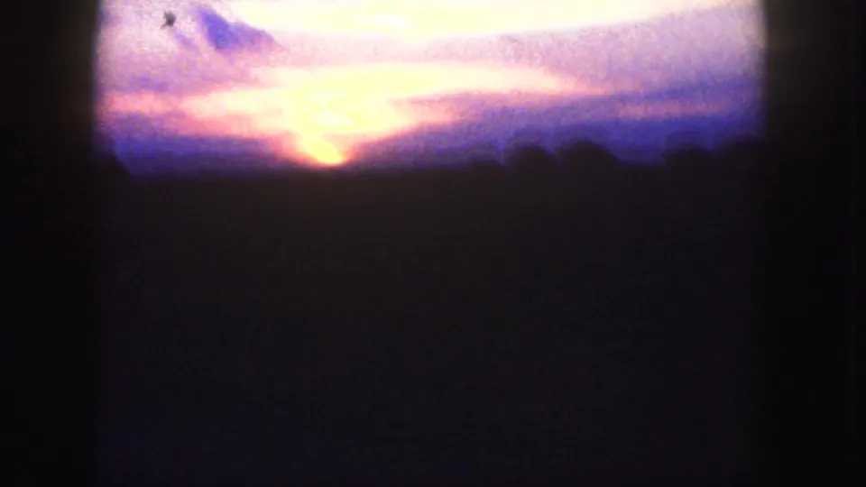 Final 1958 8mm Denver frame with a bright sunset glow, dark vertical interior edges, and a shadowed landscape foreground.