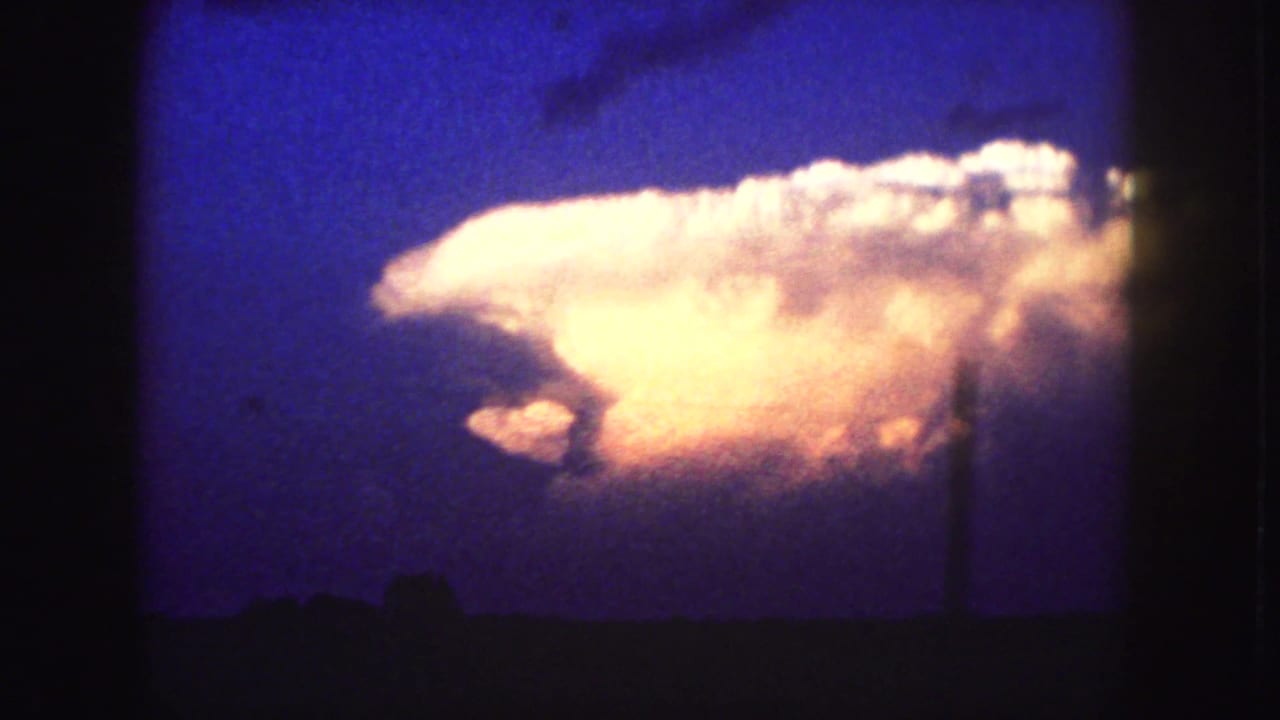 1958 Denver-area home-movie frame showing an illuminated storm cloud over a dark horizon beneath a deep blue sky.