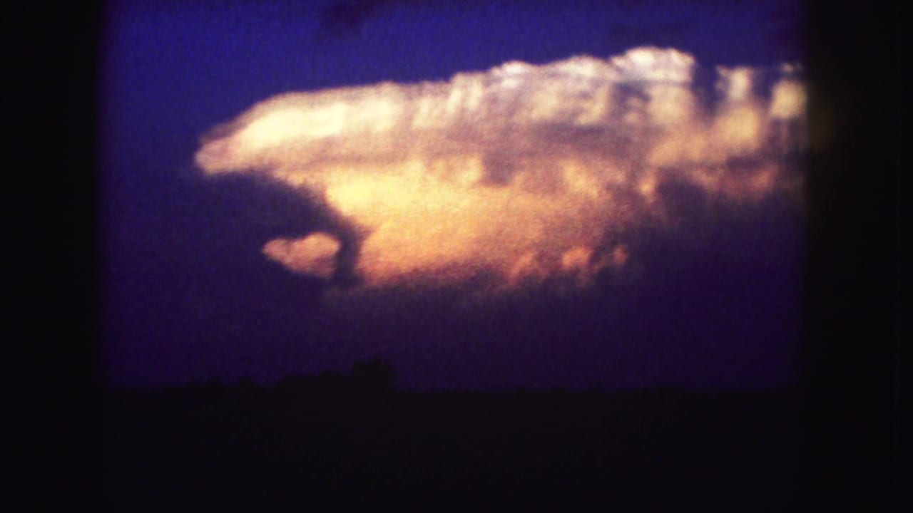 Large bright cloud hangs over a silhouetted horizon in deep blue light.