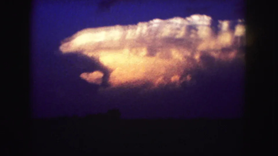 Color 8mm frame of a bright storm cloud against a deep blue sky, with the ground reduced to dark silhouettes.