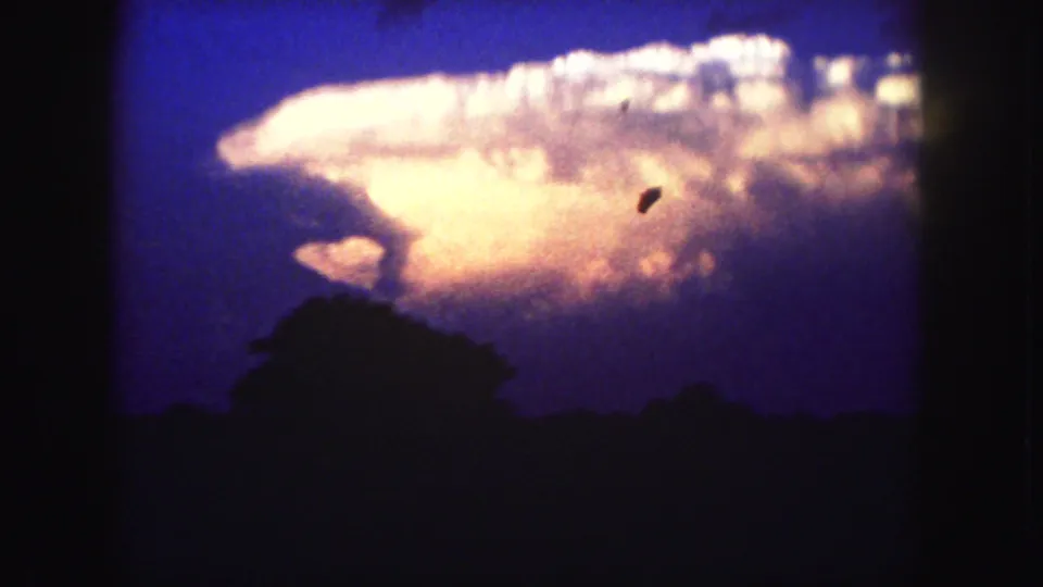 Color 8mm frame showing a glowing storm cloud above silhouetted trees, with visible gate borders and dust marks.