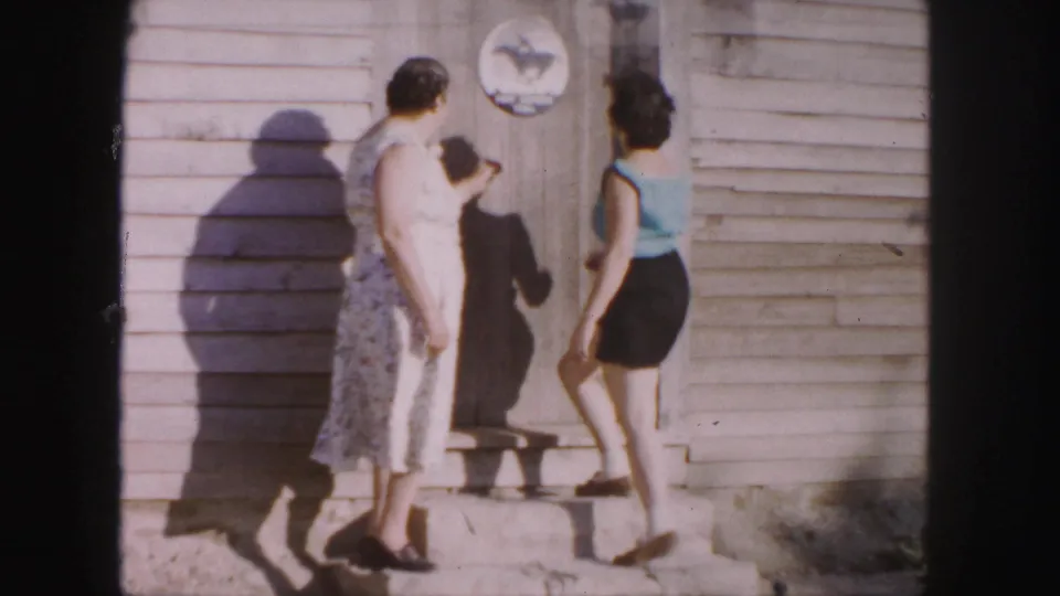 An older woman and a younger woman meet on the steps of a weathered wooden building in 1958 Denver footage.