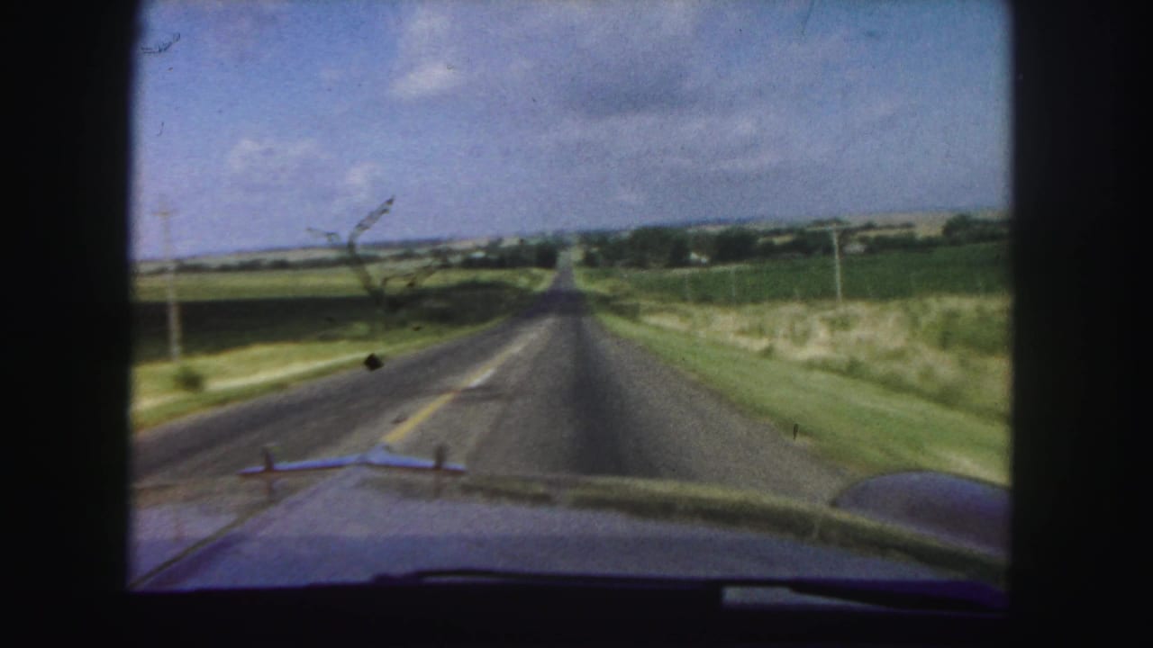 1958 8mm view from inside a car driving along a straight rural road near Denver, with fields and utility poles visible.