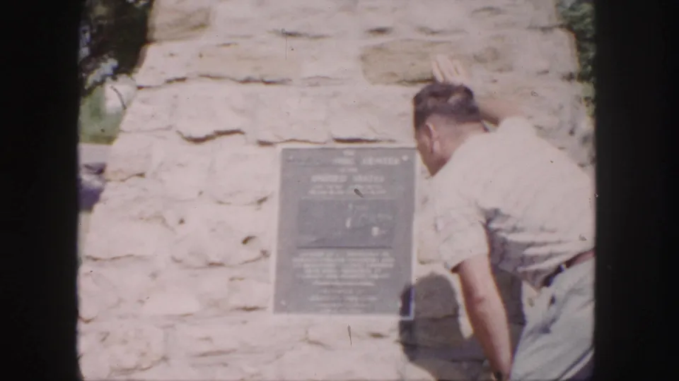 Home-movie close view of the Denver monument plaque area as a man leans toward the stone structure.