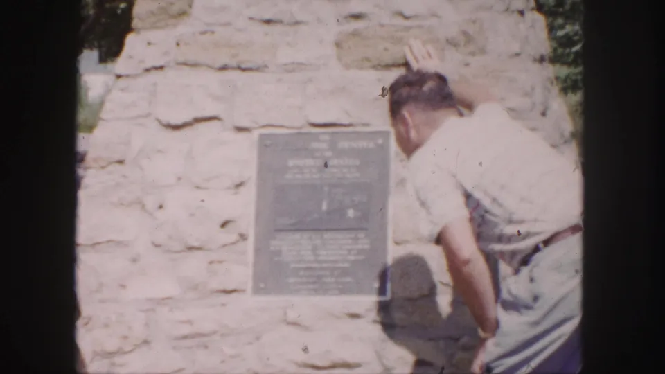 Final 1958 Denver frame showing the man beside the plaque on the stone monument, with the surface overexposed in bright sun.