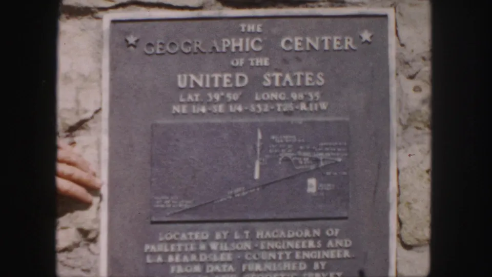 Close 1958 frame of the Geographic Center plaque, showing engraved title text, coordinates, map panel, and stone surround.