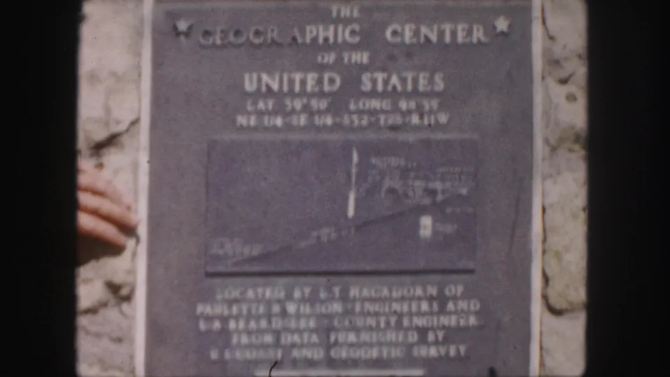 1958 8mm frame showing the Geographic Center plaque with its engraved title, map inset, and surrounding stone surface.