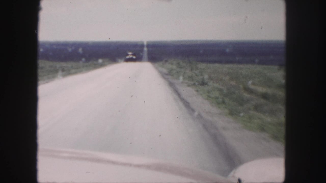 1958 8mm home-movie view near Denver of a straight rural highway stretching past grassy fields.