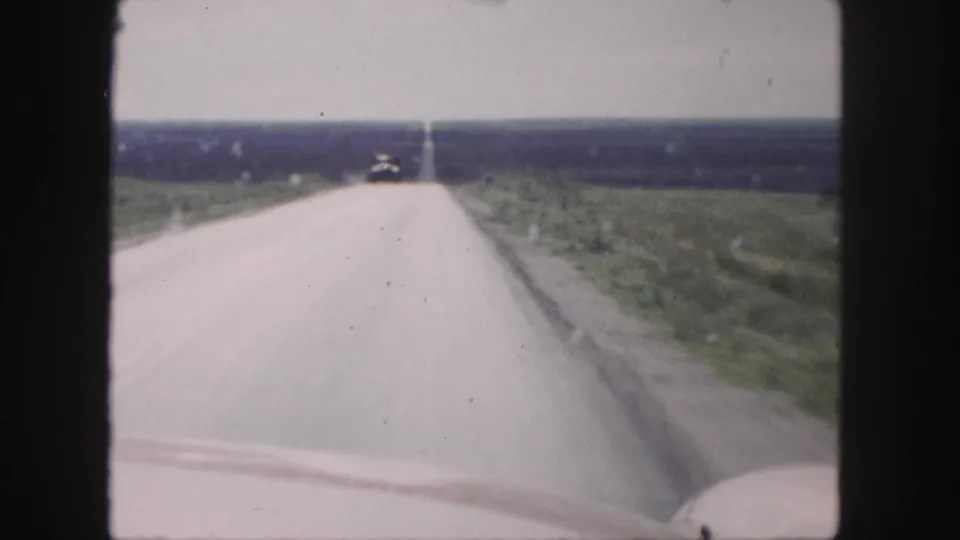 1958 8mm home-movie view near Denver of a straight rural highway stretching past grassy fields.