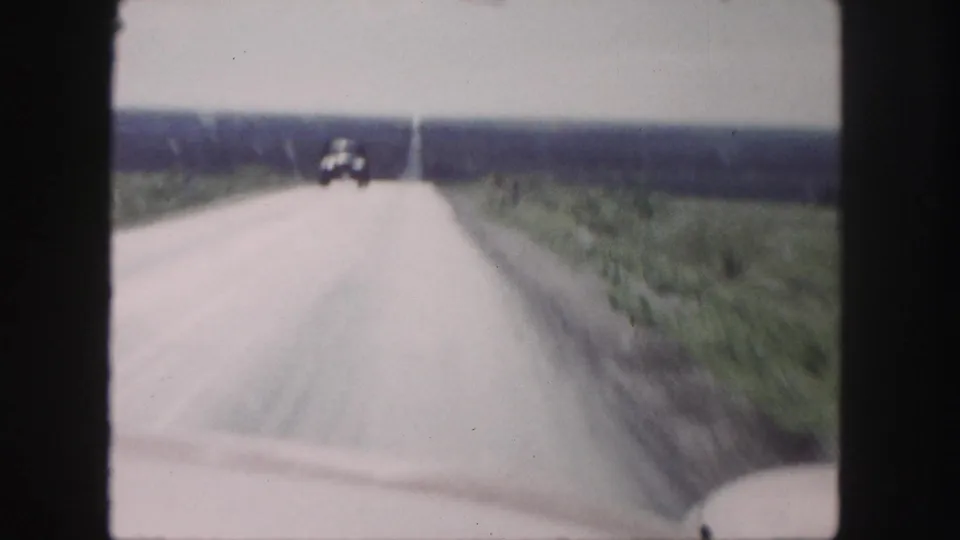 An oncoming automobile is visible far ahead on a straight rural highway in the 1958 Denver-area footage.