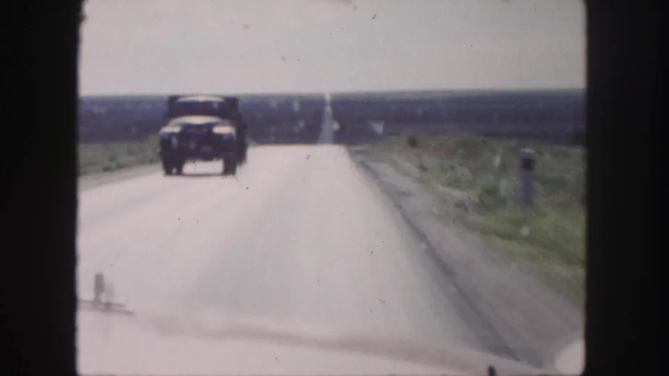 The oncoming classic automobile nears the camera on the straight rural highway near Denver in 1958.