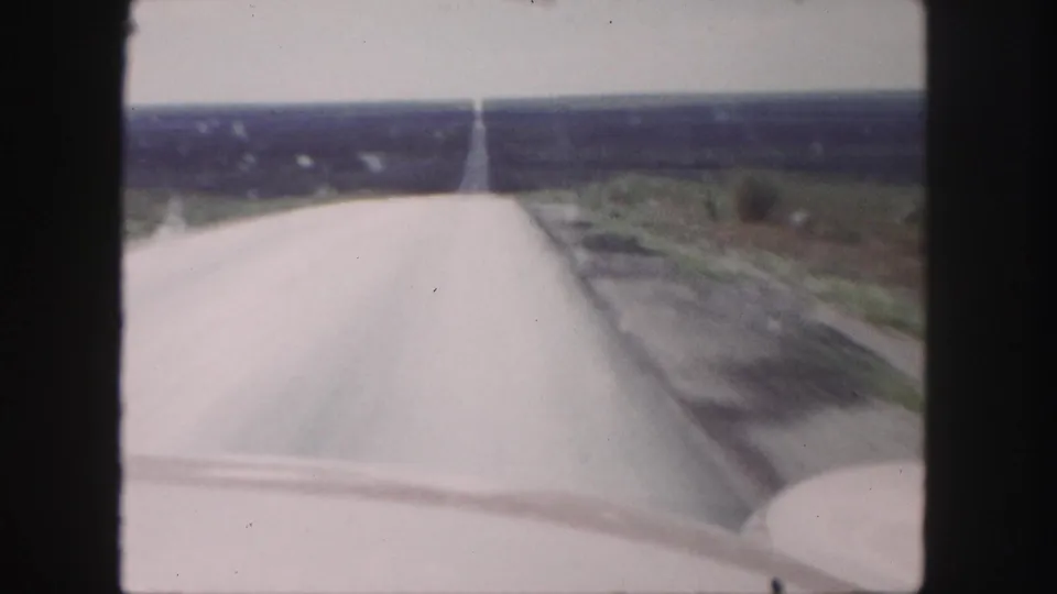 The rural highway continues into the distance after the oncoming car has passed in the 1958 home-movie shot.