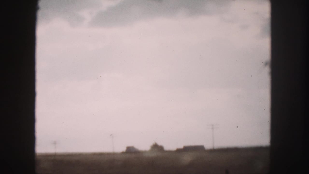 Rural horizon with distant buildings, utility poles, and fields seen through a car window.