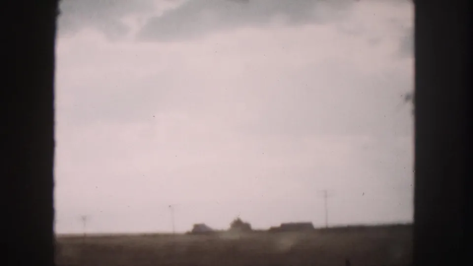A Denver-area rural landscape in 1958, seen from a moving car, with fields, utility poles, and distant farm buildings.