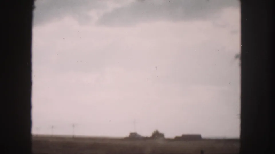 Soft 8mm view of the 1958 Denver-area roadside, with open fields, utility poles, and distant farm structures.