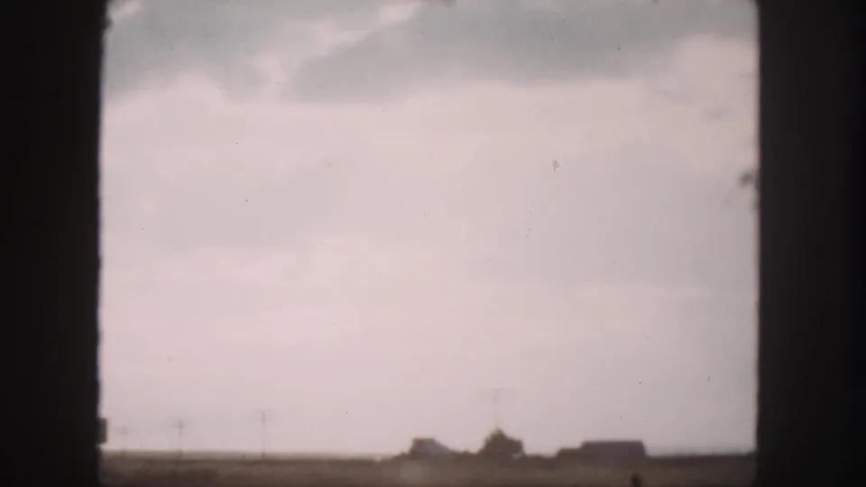 Final 1958 Denver-area road-trip frame showing a flat rural horizon, utility poles, and small buildings through the car window.