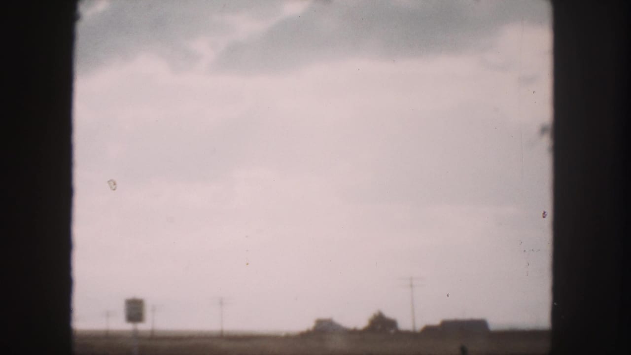 1958 Denver-area 8mm travel view with a pale sky, low horizon structures, and dark vehicle-window framing.