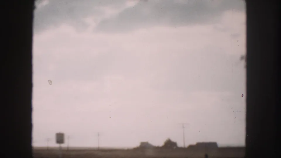 1958 Denver-area 8mm travel view with a pale sky, low horizon structures, and dark vehicle-window framing.