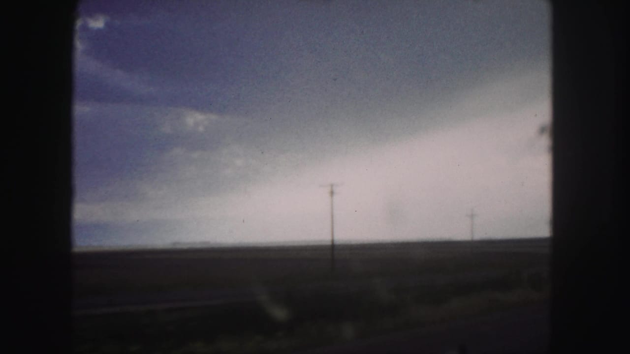 Overcast fields seen through dark window framing with a utility pole near the horizon.
