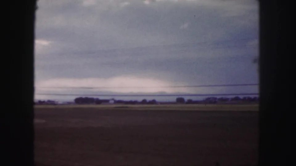 Denver-area 1958 8mm roadside shot showing a broad field, low horizon, power line, and subdued overcast sky.