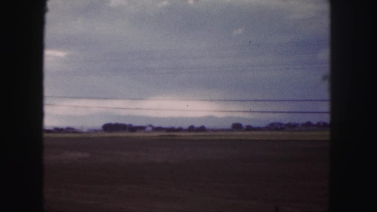 Flat open fields under a cloudy sky with power lines crossing the horizon.