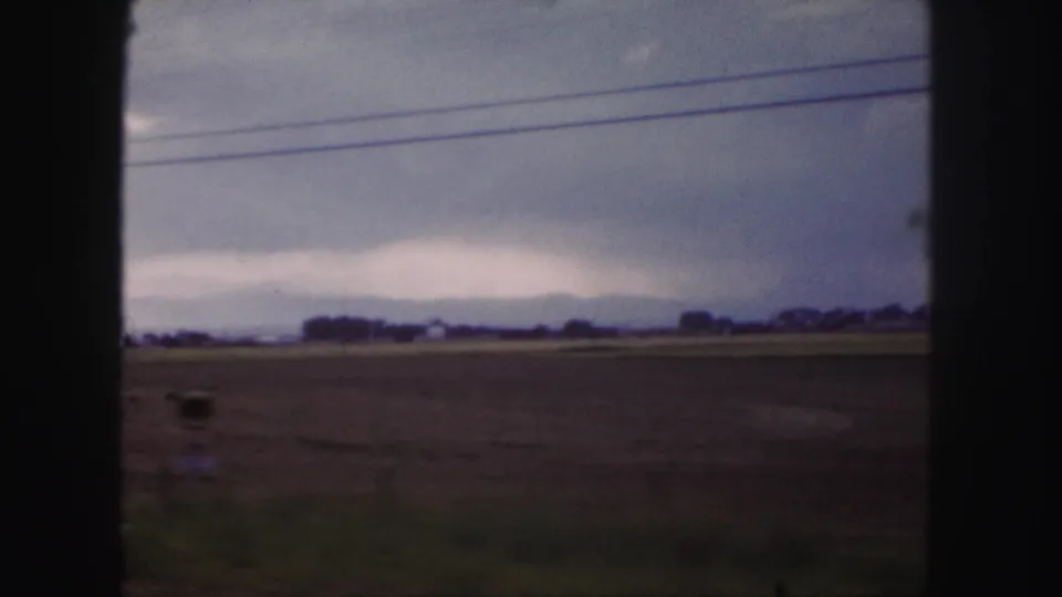 Soft 8mm frame of Colorado plains near Denver with power lines, low distant structures, and a muted cloudy sky.