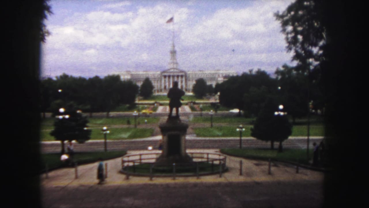 1958 Denver home-movie frame looking across Civic Center Park toward the Colorado State Capitol, with a statue and pathways in front.