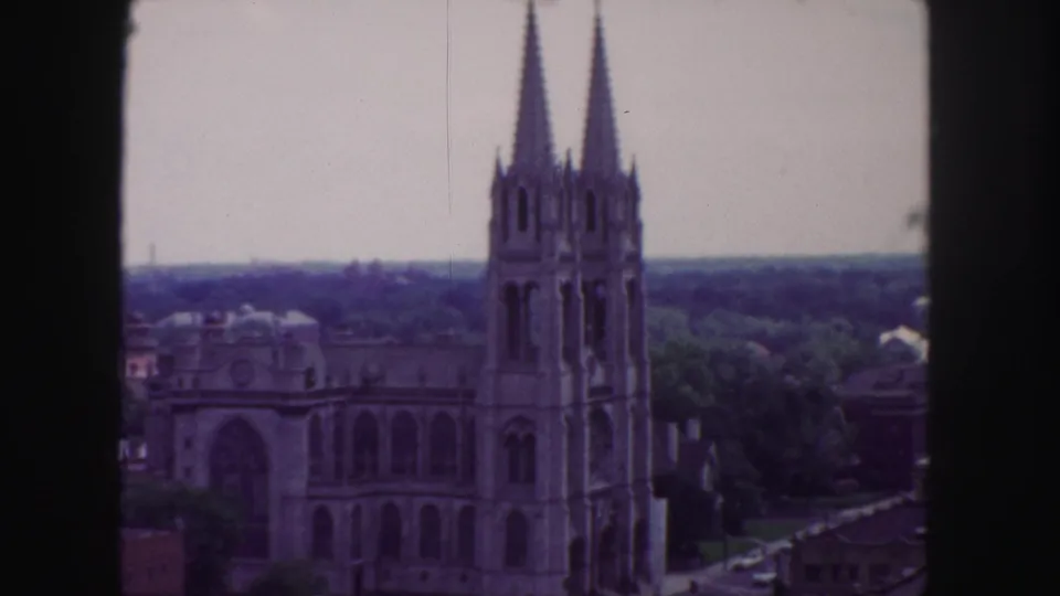 1958 Denver frame of a twin-spired church-like landmark seen from above, with trees, nearby rooftops, and softened color from 8mm film.
