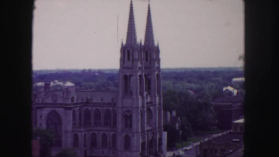 Final 1958 Denver frame showing the twin-spired Gothic cathedral from above, with trees, rooftops, hazy distance, and dark edge framing.