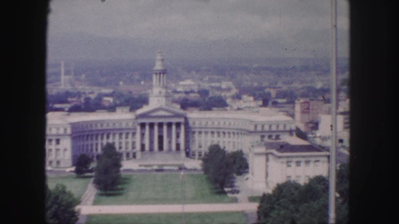 Large columned civic building with lawn and cityscape beyond.