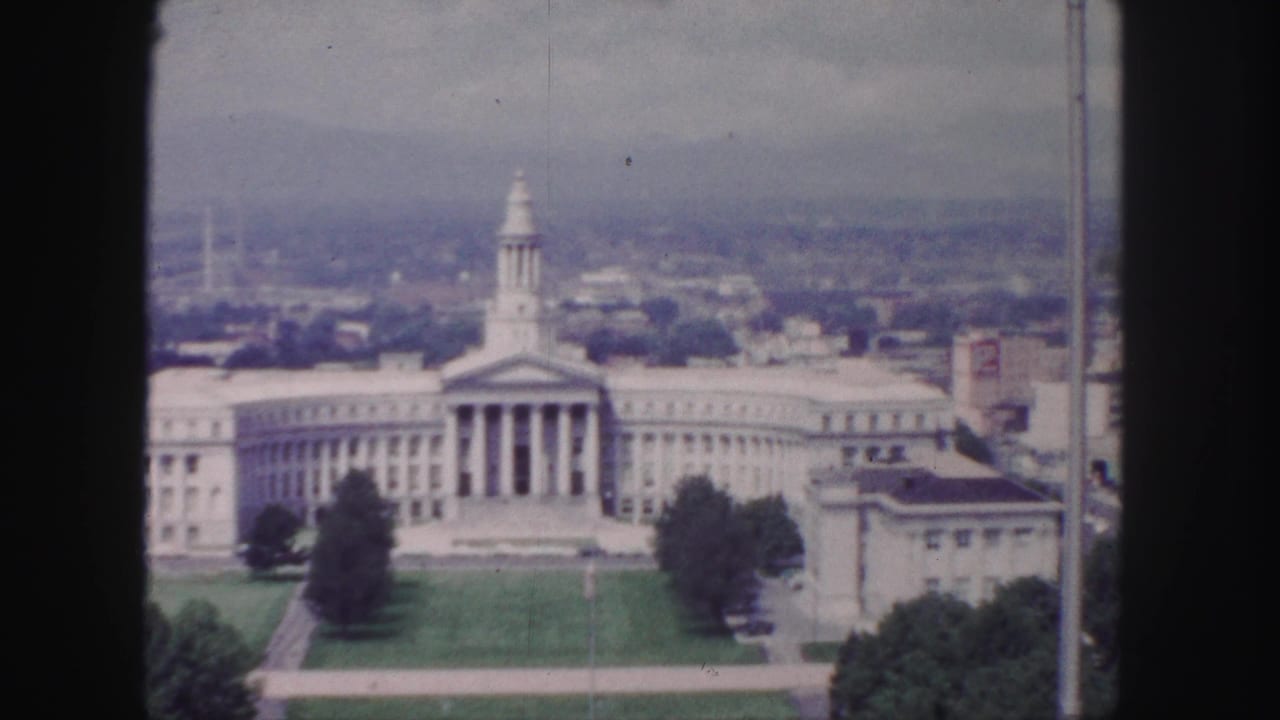 1958 Denver 8mm frame with the neoclassical building centered, its portico and wings visible above a lawn and surrounding city blocks.