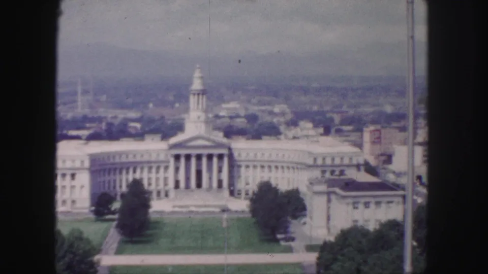 1958 Denver 8mm frame with the neoclassical building centered, its portico and wings visible above a lawn and surrounding city blocks.